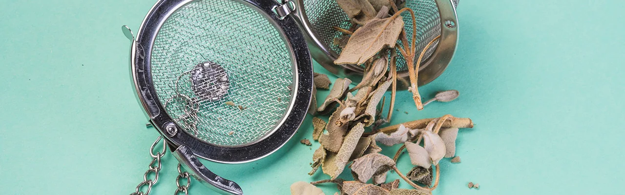 loose dried herbal tea leaves and a tea strainer on blue background