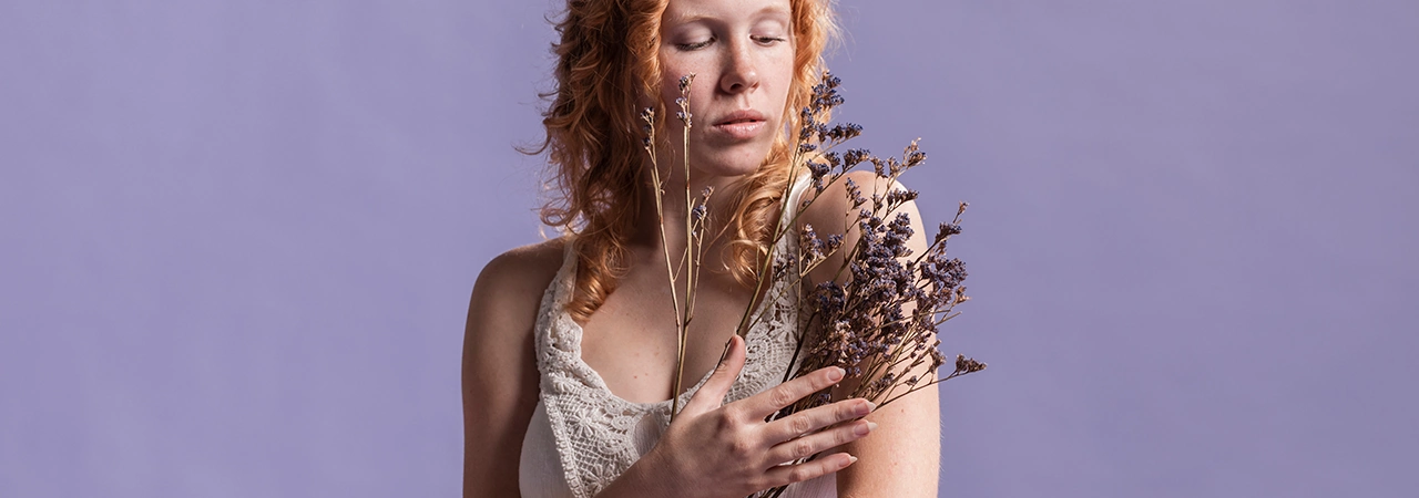 young woman with red hair holding lavender herbal bouquet, light purple background