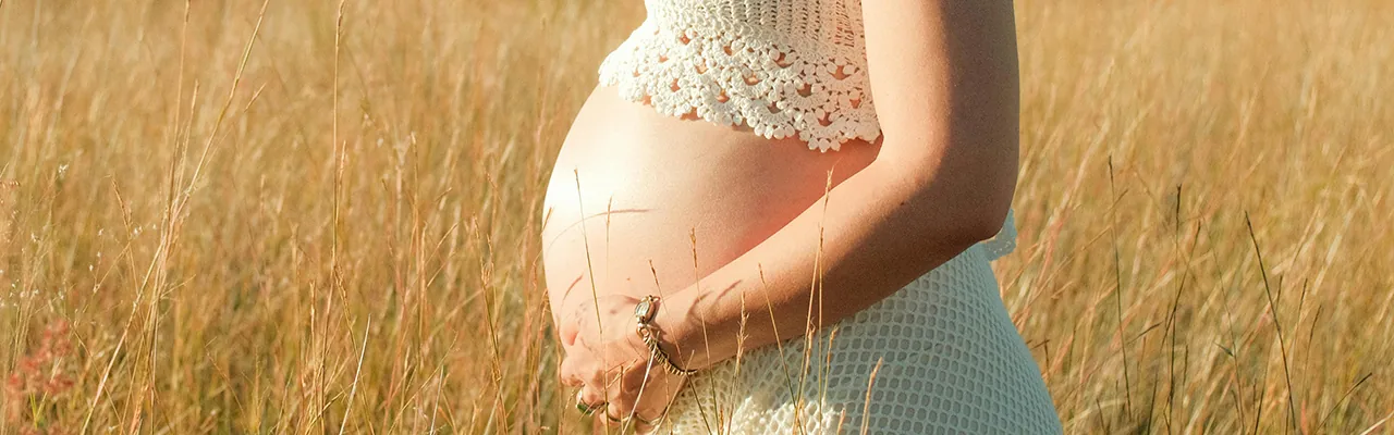 pregnant woman in white top standing in the field of wheat