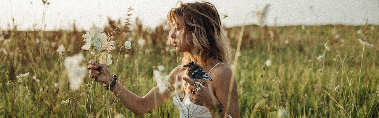 blonde woman in the field with flowers and a bird
