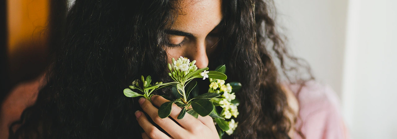 woman with dark hair holding some small white flowers with green petals in her hands
